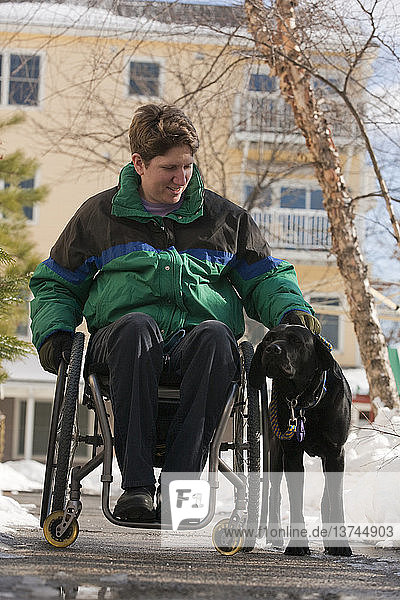 Frau mit Multipler Sklerose in einem Rollstuhl mit einem Diensthund im Winter