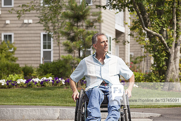 Mann mit Rückenmarksverletzung im Rollstuhl beim Überqueren eines zugänglichen Straßeneingangs