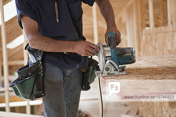 Spanischer Zimmermann bei der Arbeit mit einer Kreissäge an einer Dachplatte in einem im Bau befindlichen Haus
