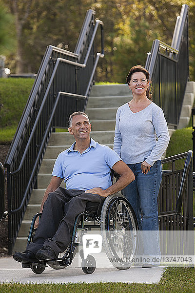 Frau mit Ehemann im Rollstuhl mit Rückenmarksverletzung auf zugänglicher Rampe stehend
