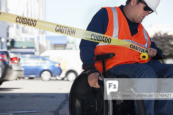 Ein Techniker im Rollstuhl zieht ein Absperrband über die Straße