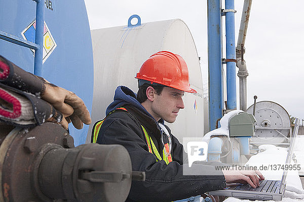 Engineer recording data on a laptop near a fuel tankers site