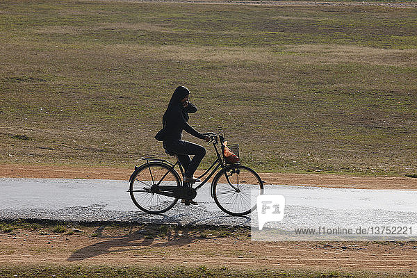 Kambodschanische Frau fährt mit dem Fahrrad auf einer kleinen Straße