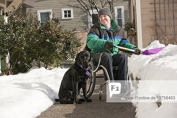 Woman with multiple sclerosis shoveling snow in a wheelchair with a service dog