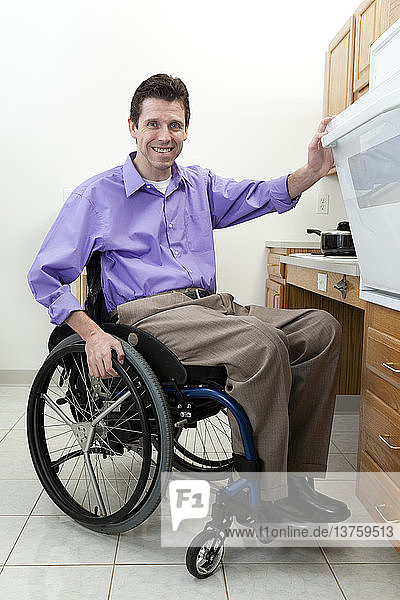 Mann im Rollstuhl mit Rückenmarksverletzung beim Öffnen des Backofens in einer barrierefreien Küche