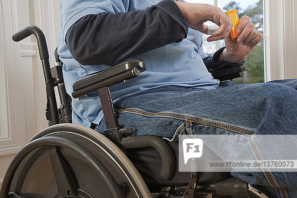 Man with spinal cord injury in a wheelchair taking pill from bottle with disabled hands