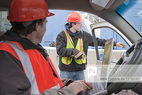 Ingenieur  der in einem Lastwagen an einem Laptop arbeitet und einem anderen Ingenieur Anweisungen gibt