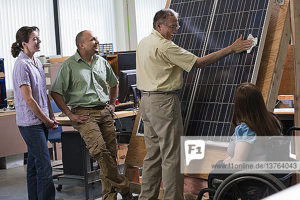 Ingenieurstudenten beobachten Professor bei der Reinigung eines Photovoltaikmoduls  um die Verbesserung des Wirkungsgrads zu demonstrieren