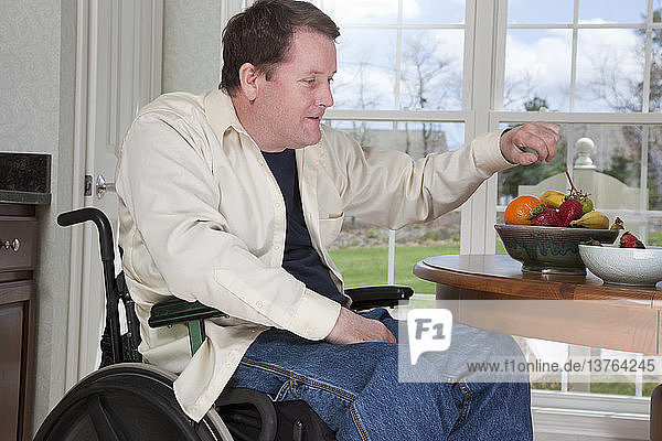 Mann mit Rückenmarksverletzung im Rollstuhl isst zu Hause frisches Obst