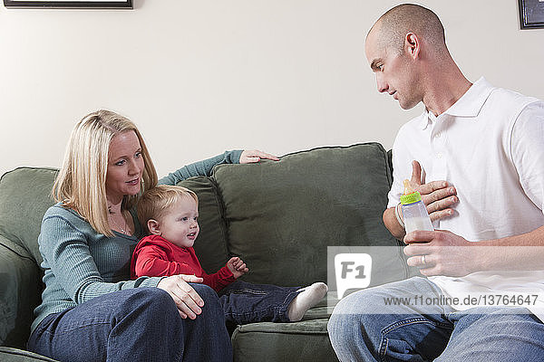 Mann gebärdet das Wort ´Please´ in amerikanischer Zeichensprache  während er seinen Sohn bittet  Milch zu trinken