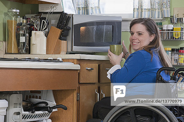 Frau mit Spina Bifida im Rollstuhl benutzt ihre Mikrowelle in der barrierefreien Küche