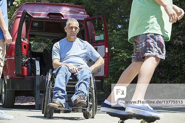 Man with spinal cord injury in wheelchair watching his son on skateboard