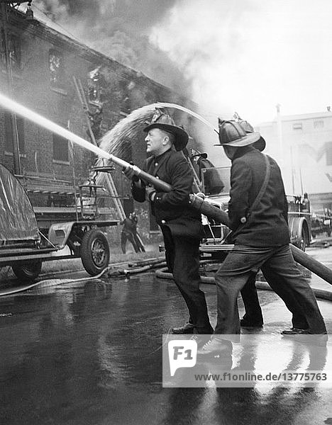 Chicago  Illinois: c. 1935 Three firemen directing a hose at a large building on fire.