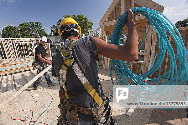 Zimmermann beim Abwickeln eines Luftschlauchs im zweiten Stock eines im Bau befindlichen Hauses