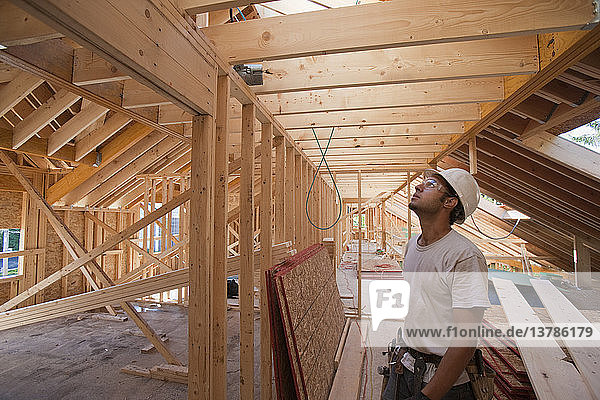 Hispanischer Zimmermann betrachtet das Dach im Obergeschoss eines im Bau befindlichen Hauses