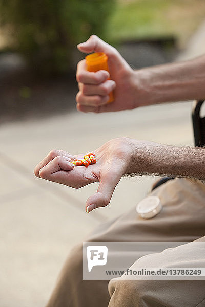 Mann mit Friedreich´s Ataxie hält Tabletten mit degenerierten Händen