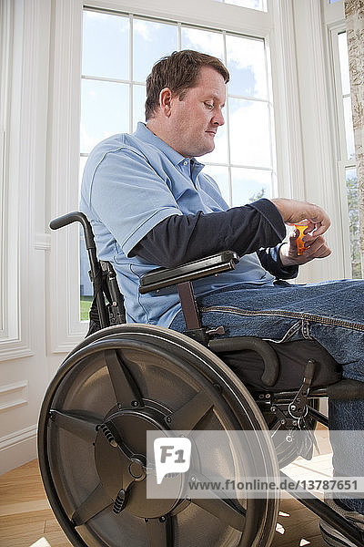 Mann mit Rückenmarksverletzung im Rollstuhl nimmt mit behinderten Händen Pille aus Flasche