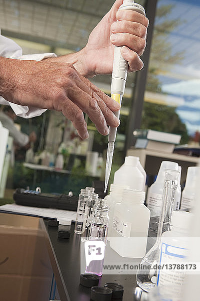 Wissenschaftlerin bei der Verwendung einer kalibrierten Pipette mit Probenflaschen im Labor einer Wasseraufbereitungsanlage