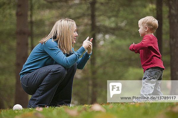 Frau gebärdet das Wort ´Game´ in amerikanischer Zeichensprache  während sie mit ihrem Sohn in einem Park kommuniziert