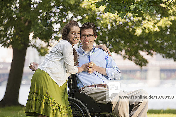 Schwangere Frau umarmt ihren Mann im Rollstuhl mit einer Rückenmarksverletzung