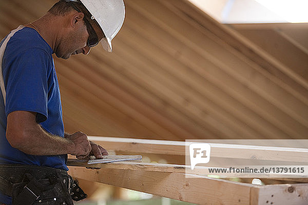 Ein spanischer Zimmermann misst den Winkel eines Sparrens an einem im Bau befindlichen Haus