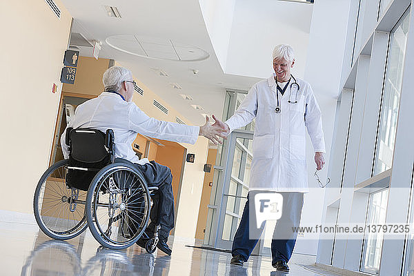 Arzt mit Muskeldystrophie im Rollstuhl gibt einem anderen Arzt die Hand