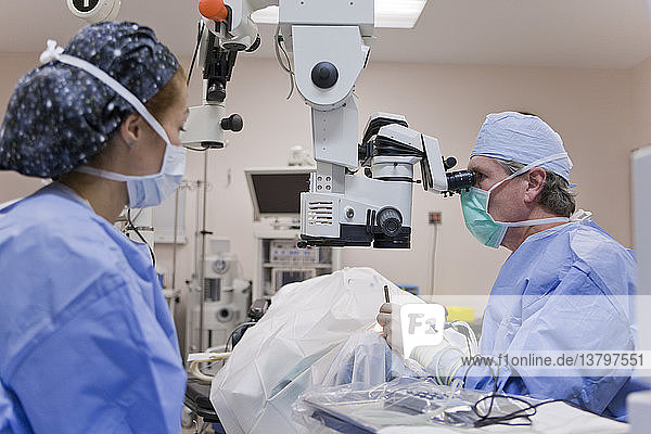 Arzt schaut in ein Mikroskop und benutzt ein Cracker-Instrument und ein Phako-Handstück während einer Kataraktoperation