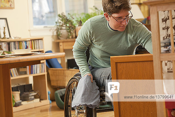 Frau mit Multipler Sklerose im Rollstuhl holt Tischdecken aus einem zugänglichen Schrank