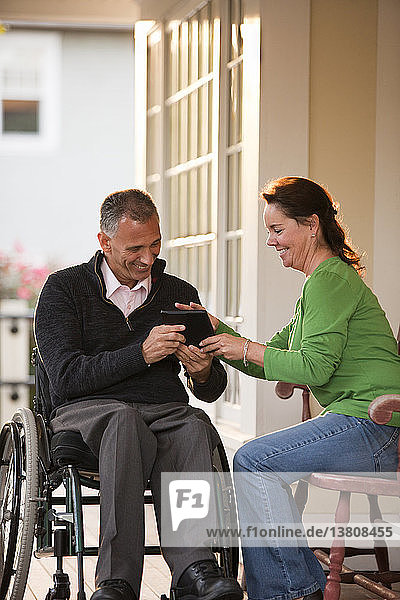 Woman and her husband in a wheelchair in front of their home using a digital tablet