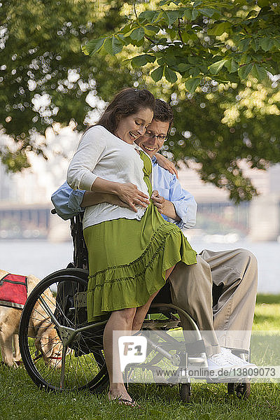 Man with a spinal cord injury in a wheelchair feeling his wife´s baby belly