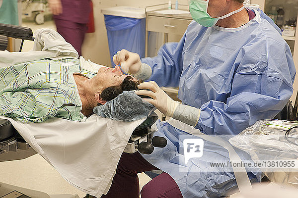 Ophthalmologe nimmt das Tuch vom Auge und reinigt den Patienten nach der Operation