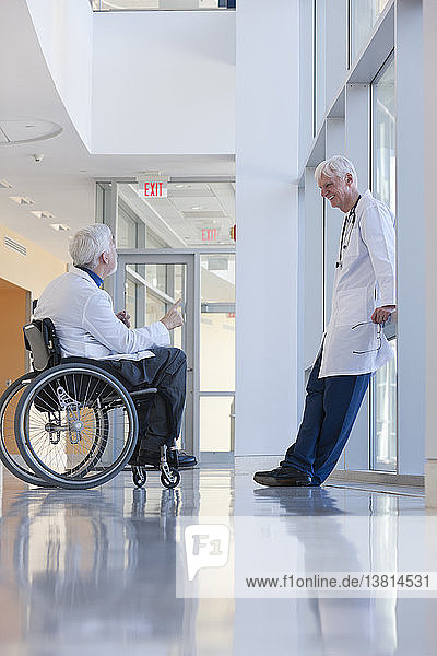 Arzt mit Muskeldystrophie im Rollstuhl im Gespräch mit einem anderen Arzt