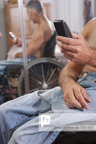 Mann mit Rückenmarksverletzung im Rollstuhl  der ein Mobiltelefon benutzt