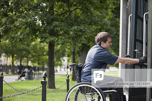 Mann mit Rückenmarksverletzung im Rollstuhl fährt durch die Tür eines öffentlichen Parkplatzes