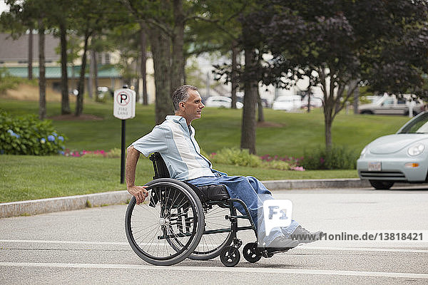 Mann mit Querschnittslähmung im Rollstuhl beim Überqueren einer begehbaren Straße