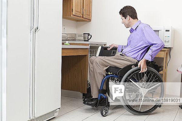 Mann im Rollstuhl mit Rückenmarksverletzung öffnet zugänglichen Geschirrspüler