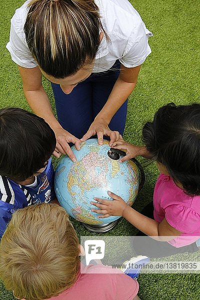 Kindergärtnerin zeigt Länder auf einem Globus.