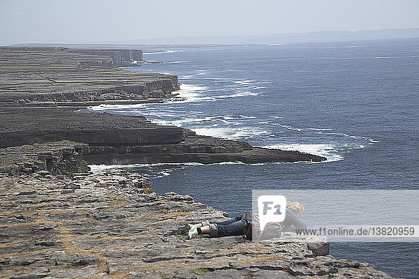 Woman peering over edge of sheer cliff D´n Aengus fort Inishmore  Aran Islands  County Clare  Ireland
