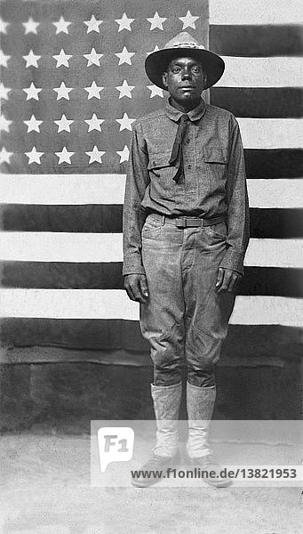 United States: c. 1916 An African American soldier in uniform in front of an American flag.