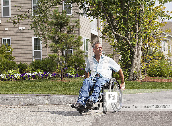 Mann mit Rückenmarksverletzung im Rollstuhl beim Überqueren eines zugänglichen Straßeneingangs