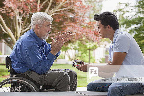 Engineer with muscular dystrophy and diabetes in his wheelchair talking with design engineer about microchips on circuit board