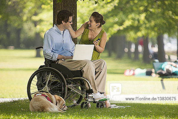 Mann im Rollstuhl mit schwangerer Frau genießt Elektronik in einem Park