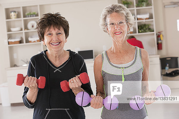 Porträt von zwei älteren Frauen  die in einem Fitnessstudio mit Hanteln trainieren