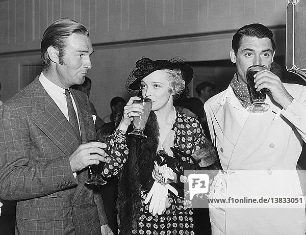 Hollywood  California: c. 1936 Movie stars Randolph Scott  Virginia Bruce and Cary Grant enjoying beverages at a Hollywood event.