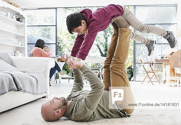 Father lifting son with legs on living room floor