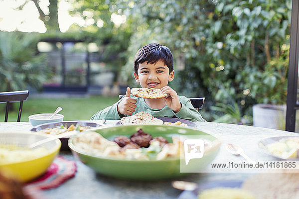 Portrait happy boy eating naan bread at patio table