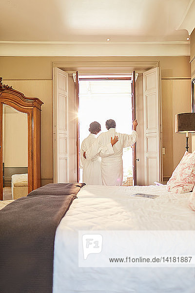 Affectionate couple in spa bathrobes standing at hotel balcony doorway