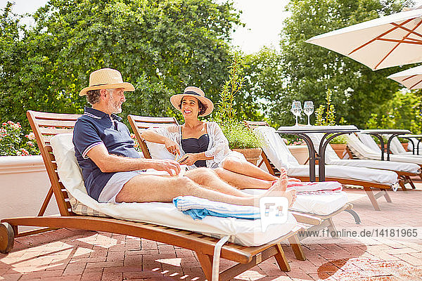 Mature couple relaxing on lounge chairs at sunny poolside