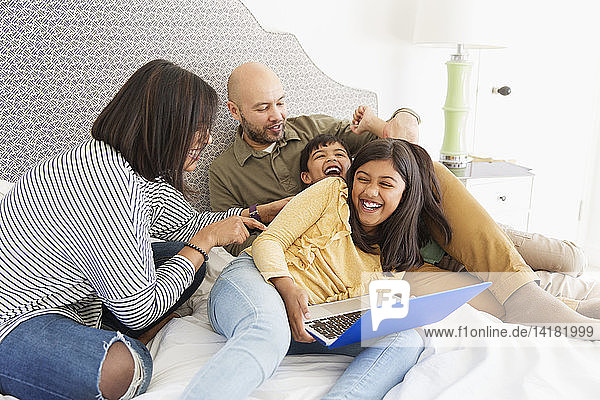 Playful family with laptop on bed