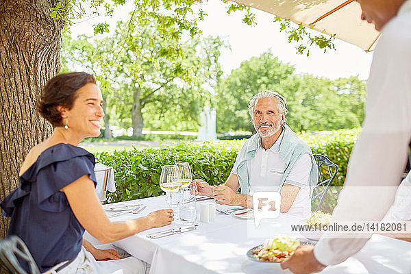 Waiter serving food to mature couple dining at patio table